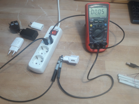 Ein Digitales Multimeter ist in Serie mit einem Handynetzteil geschalten und in die Steckdose eingesteckt. Es zeigt 0,05mA.